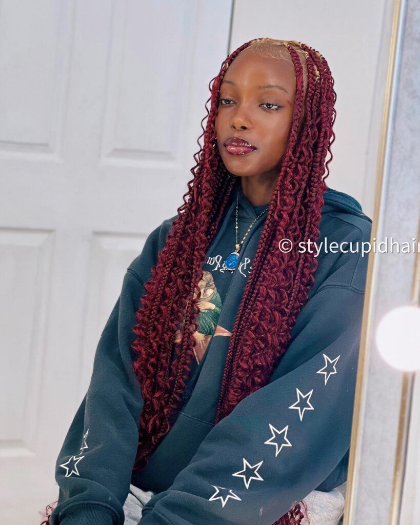 Long burgundy knotless braids with curly ends and neat parted sections.