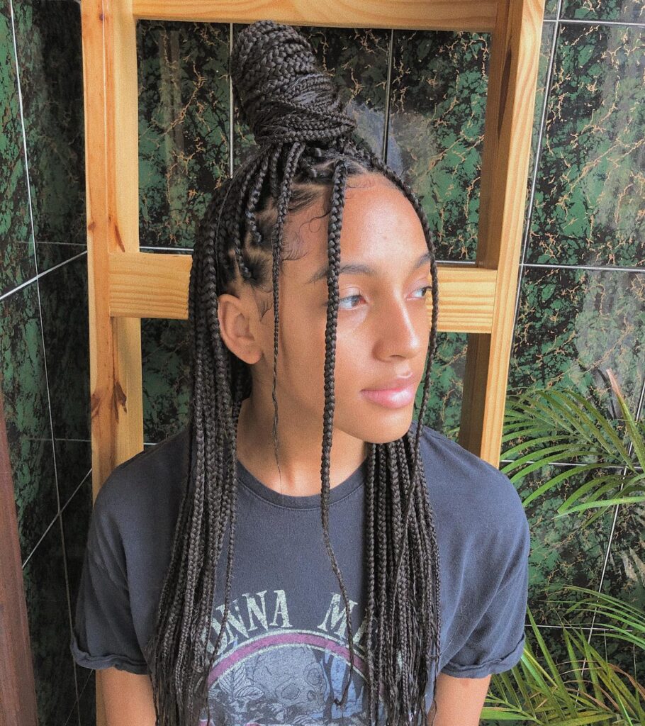 Medium length box braids styled in a half up bun with long braids left down.