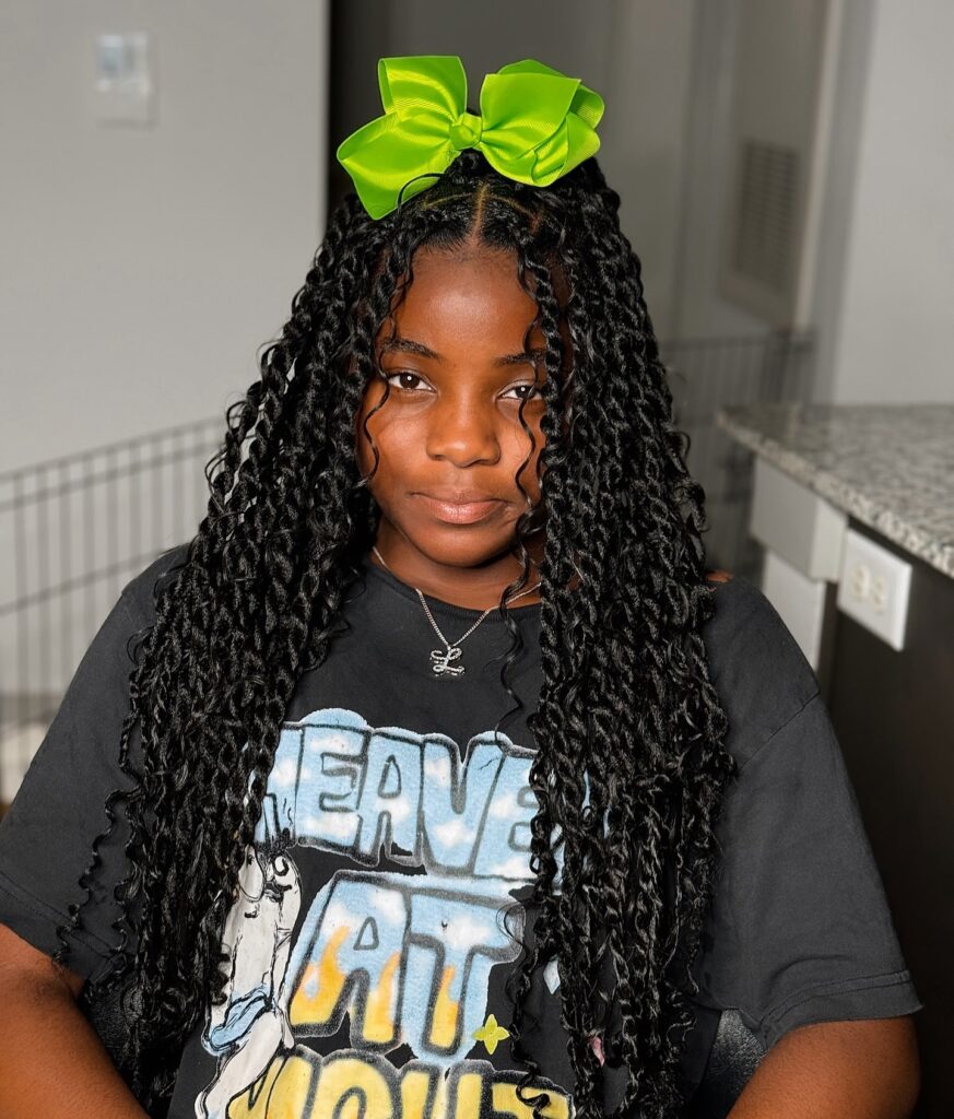 Chunky twist braids with curly ends styled with a bright green bow on top.