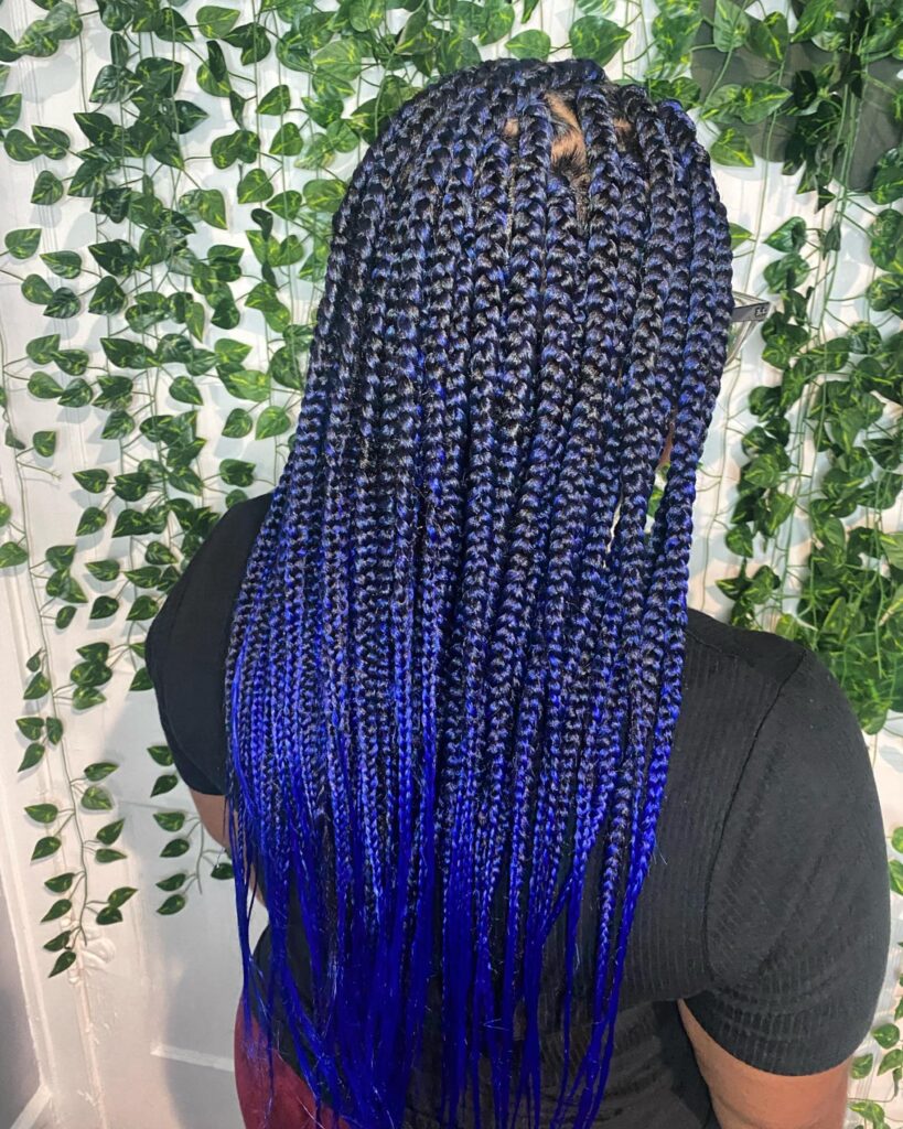 Long box braids with dark roots and bright blue dip dyed ends creating a gradient look.
