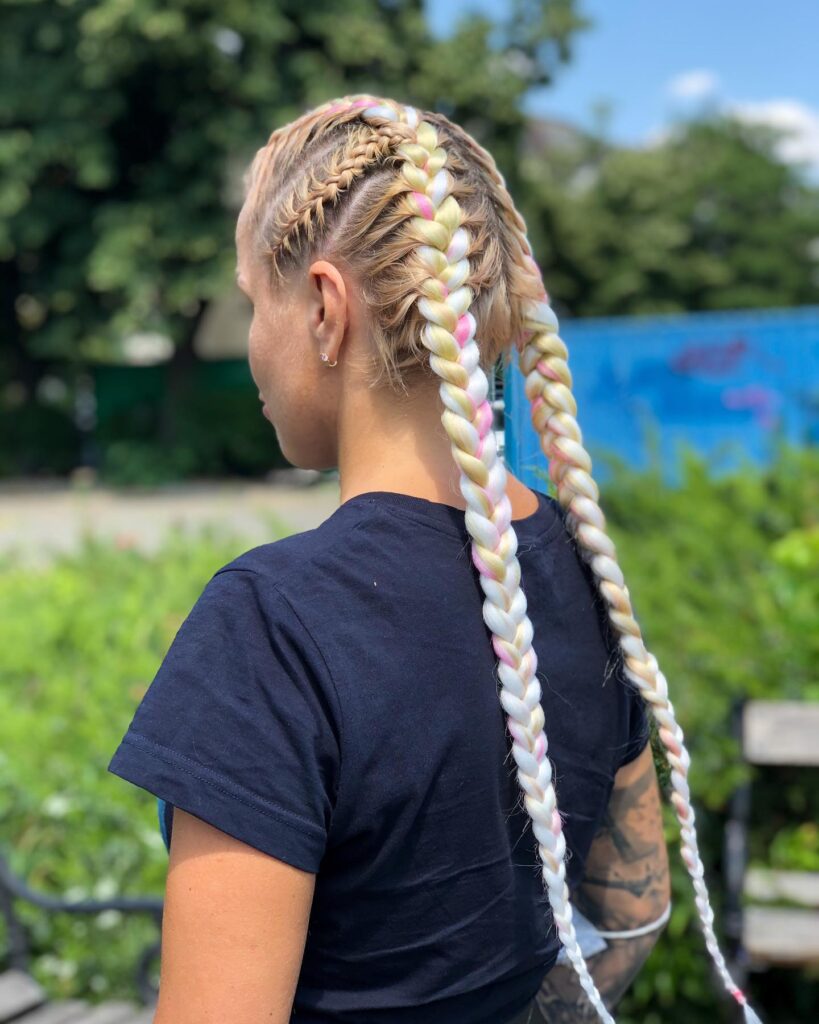 Two long blonde braids with soft pastel pink accents woven through.