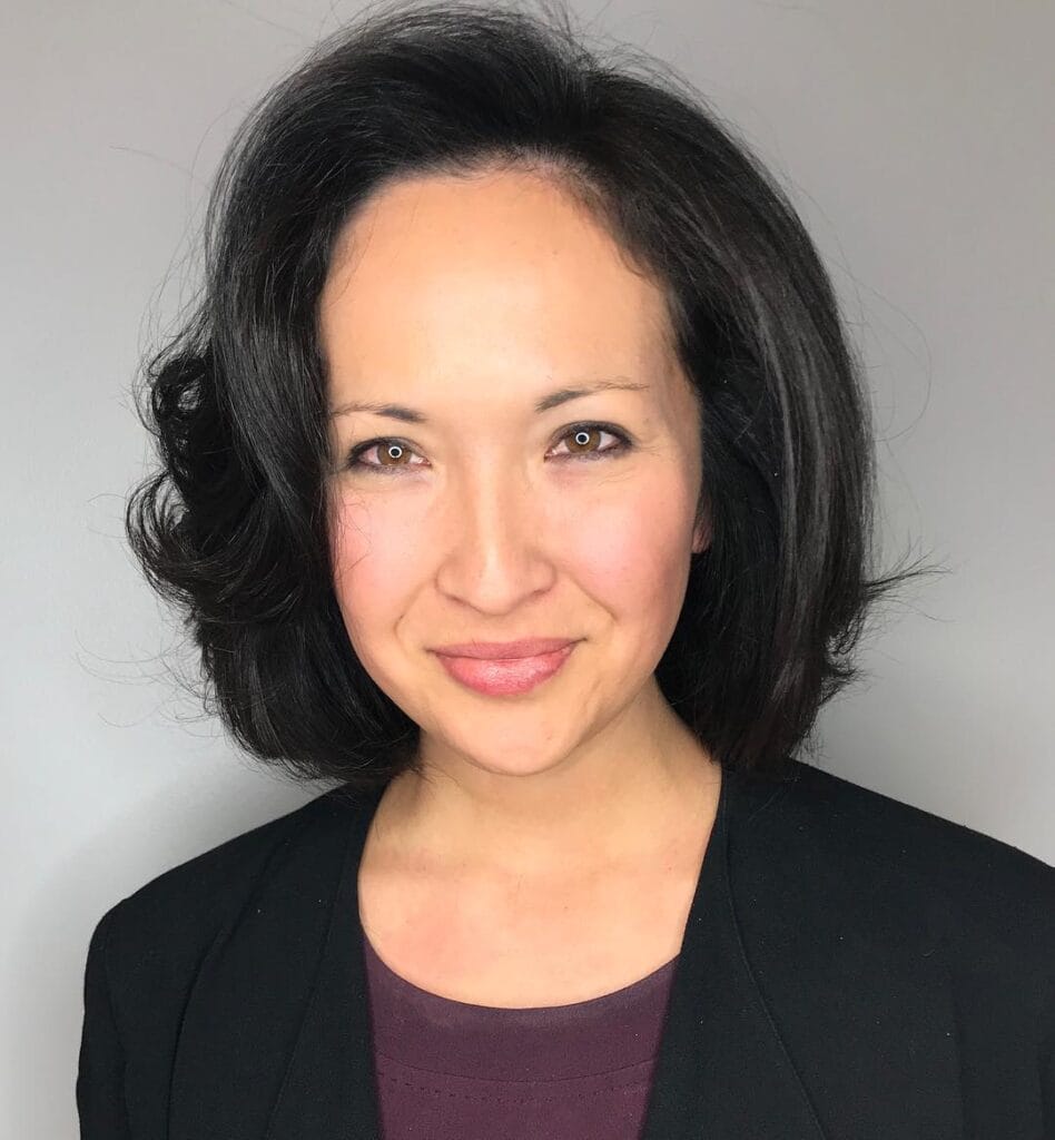 A woman with a voluminous chin length dark brown bob styled with a deep side part and flipped ends.