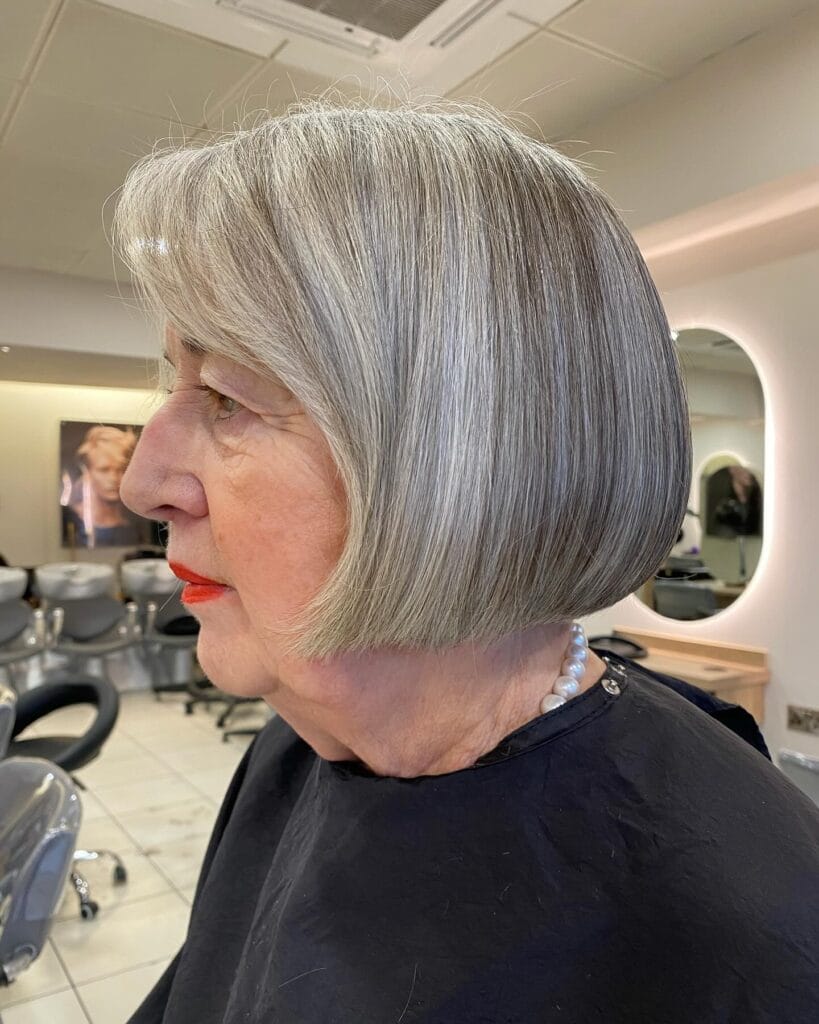 A woman with natural salt and pepper hair showcases a sleek chin length blunt bob with a sharp straight edge.