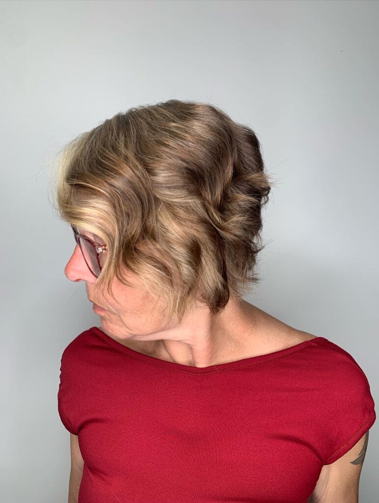 A woman showing a side profile of a wavy ash brown bob with a bright blonde money piece in the front.