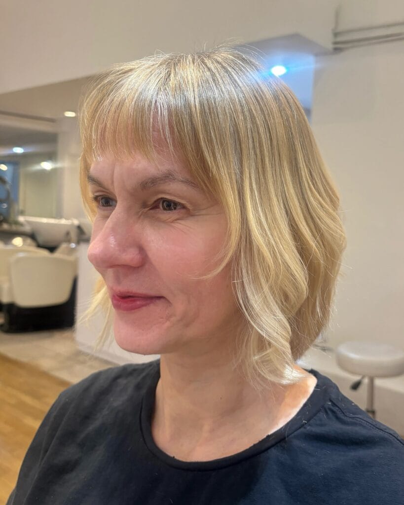 A woman with a wavy chin length blonde bob featuring light wispy bangs.