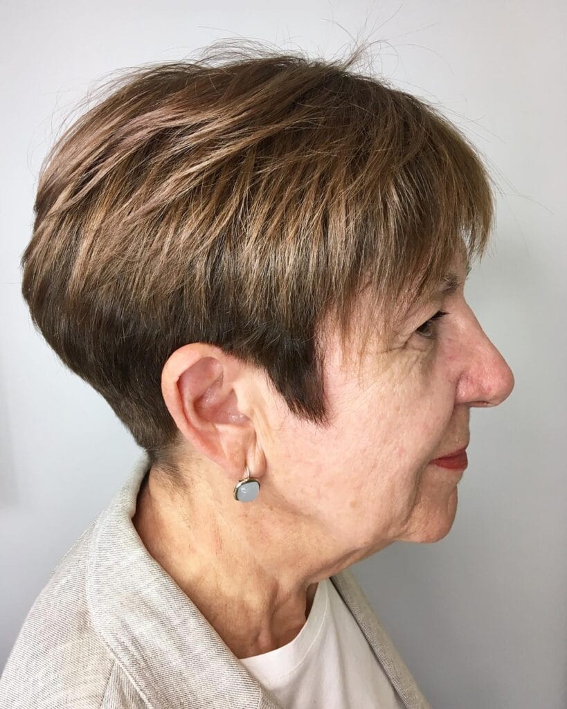 A woman showing a side profile of a short textured pixie cut in a warm brown color with wispy bangs.