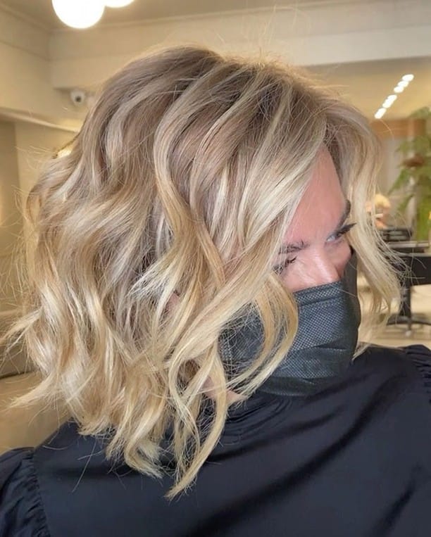 A woman with shoulder length wavy blonde hair featuring bright highlights and a voluminous side part.