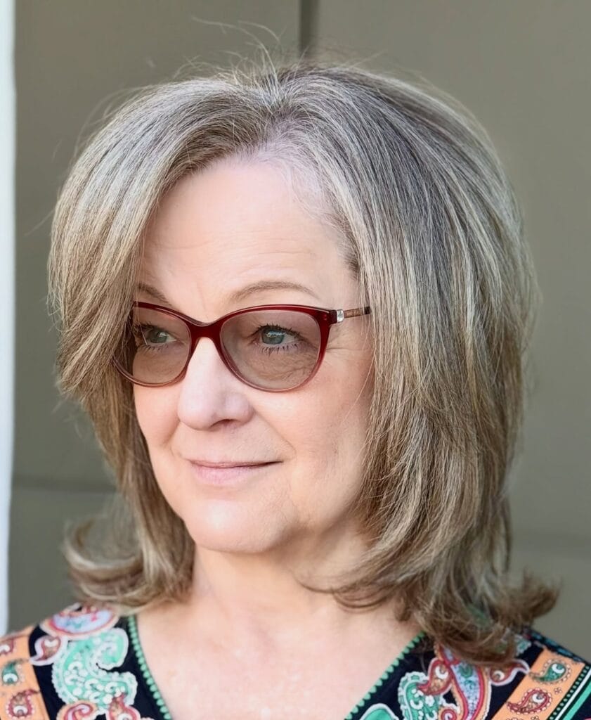 A woman with ash blonde layered hair wears a voluminous mid length shag with side swept bangs and flipped ends.