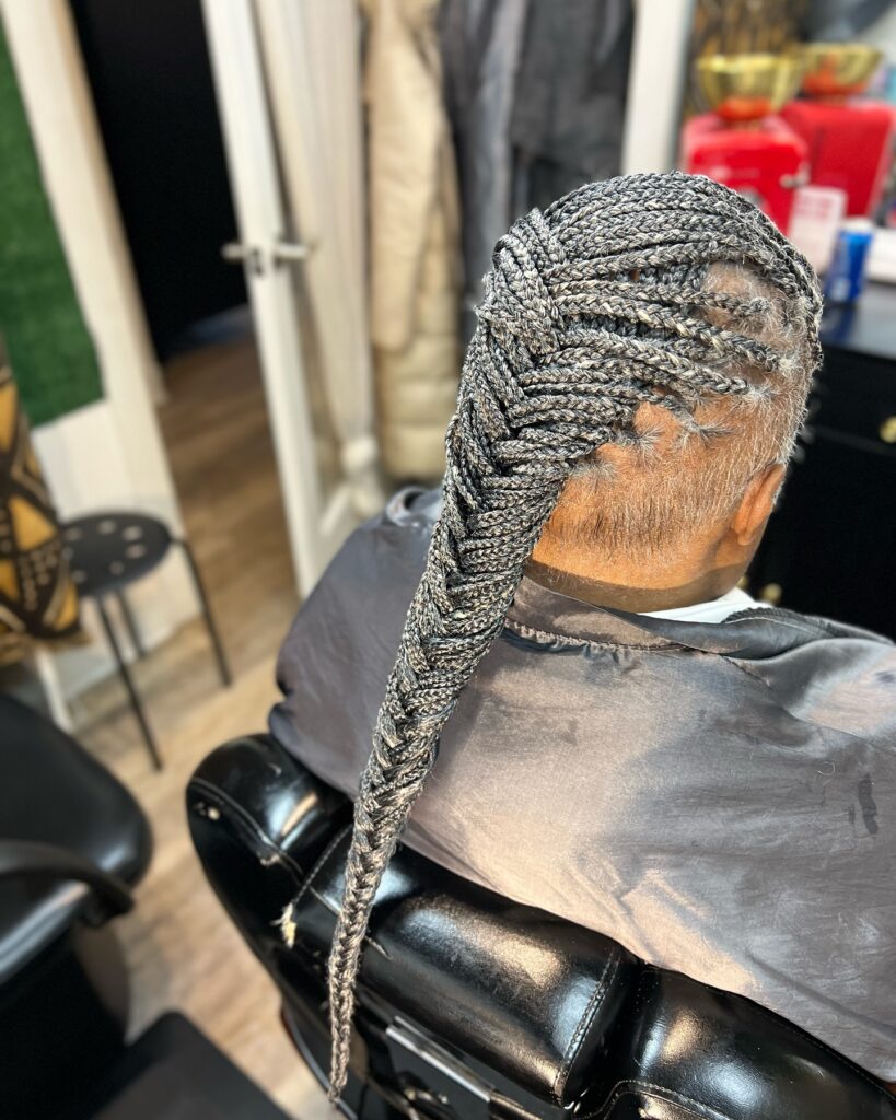 A woman from the back showing a long and thick fishtail braid created from smaller grey and black braids.