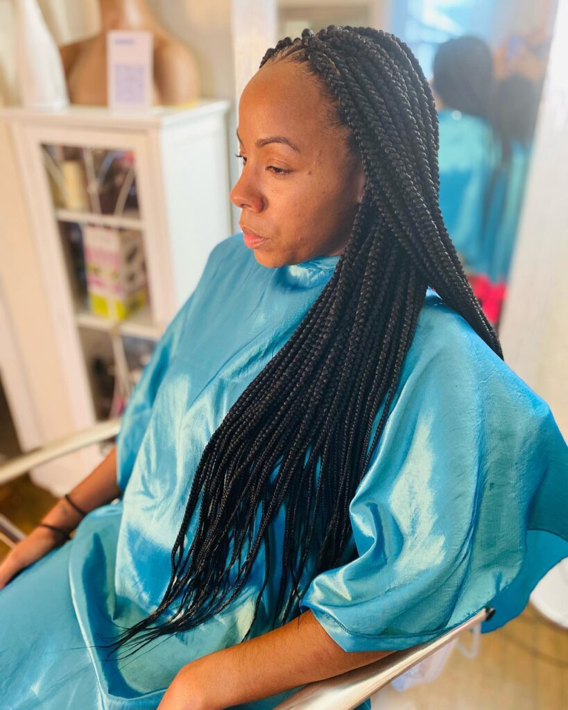 A woman in a blue salon cape showing off her long waist length knotless braids in a deep natural black color.