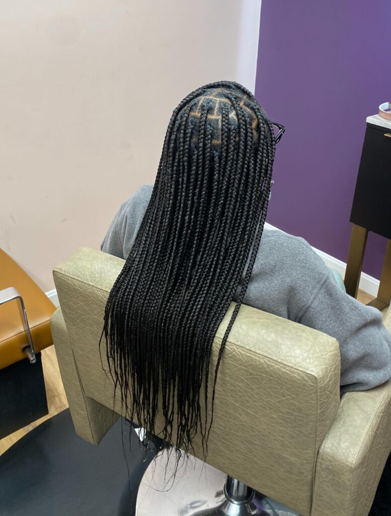 A back view of a woman sitting in a salon chair showcasing her long midnight black box braids with precise square partings.