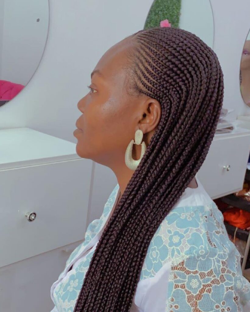 A woman in profile showing long dark mahogany cornrows that transition into straight braided extension.