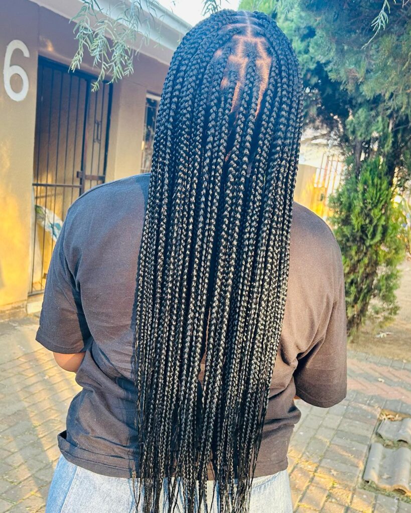 A back view of a woman featuring long waist-length knotless box braids in a rich natural black color.