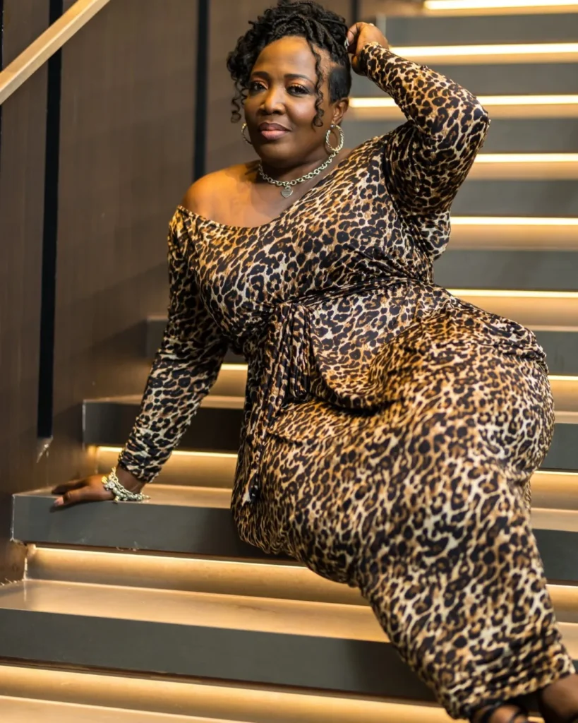 A woman sitting on stairs wearing a leopard print dress and sporting a side swept loc hairstyle with tapered sides.