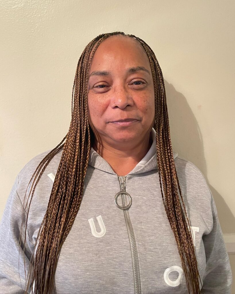 A woman smiling with long honey brown micro braids parted down the middle.
