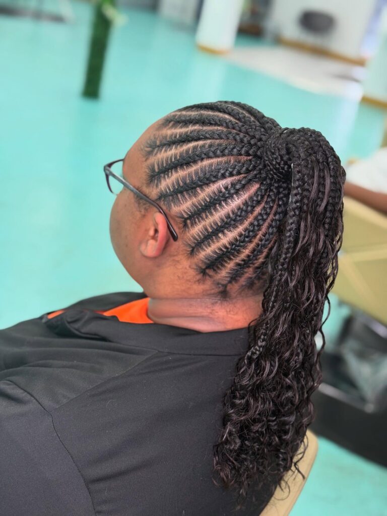 A woman in profile showing off sleek black cornrows braided into a high ponytail with long curly ends.