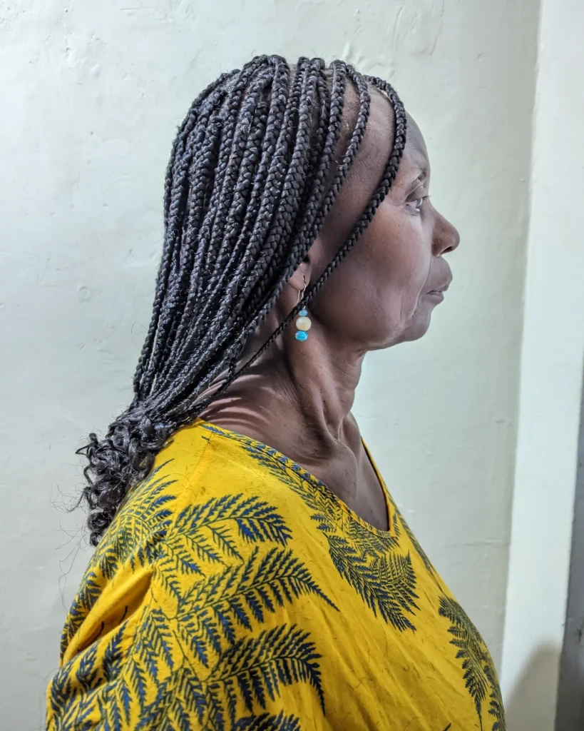 A woman with medium length black box braids featuring curly ends and a side part.