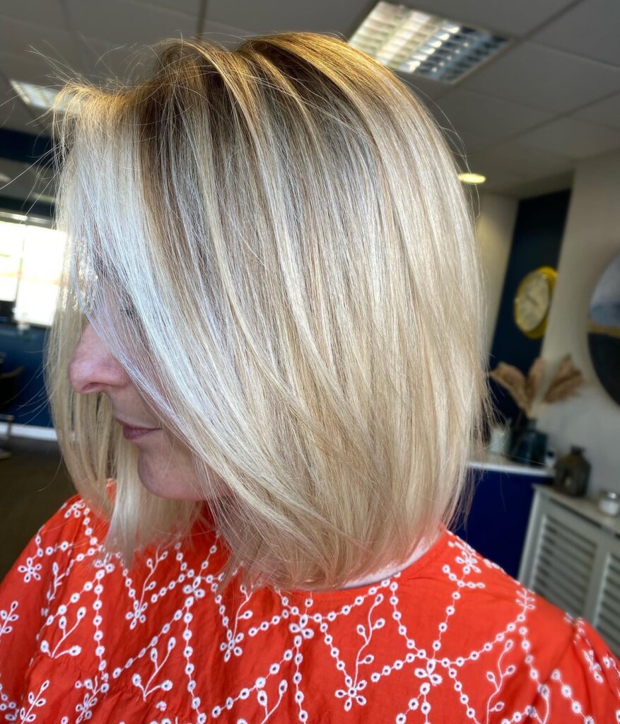 A woman seen in profile showing a straight, shoulder-length blonde blunt bob with subtle layers framing her face.