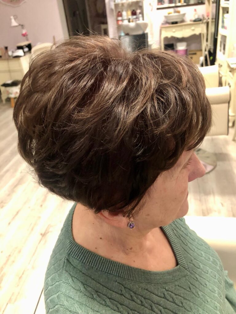 A woman with a short voluminous layered bob in a rich chocolate brown color shown from a side profile view.