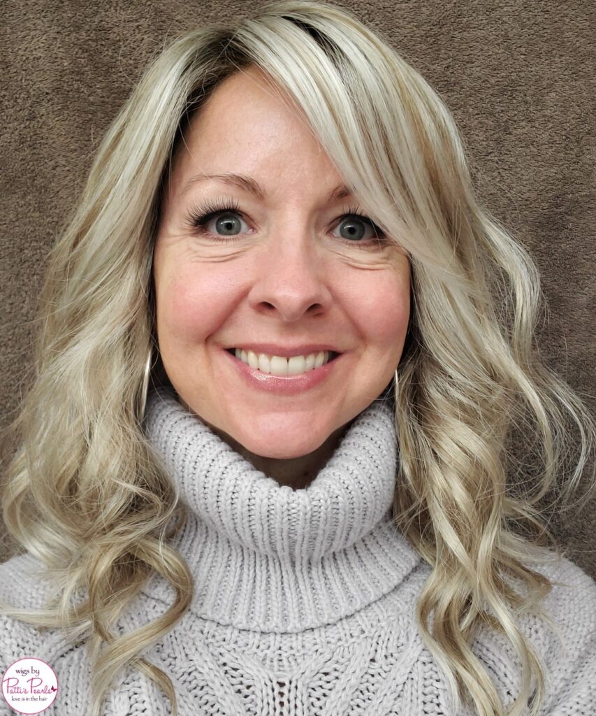 A smiling woman with shoulder length platinum blonde hair styled in soft ringlet curls and a side swept fringe.