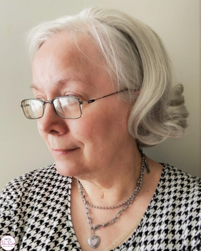 A woman with silver glasses wearing her bright white hair in a chin length bob with tight curls at the ends.