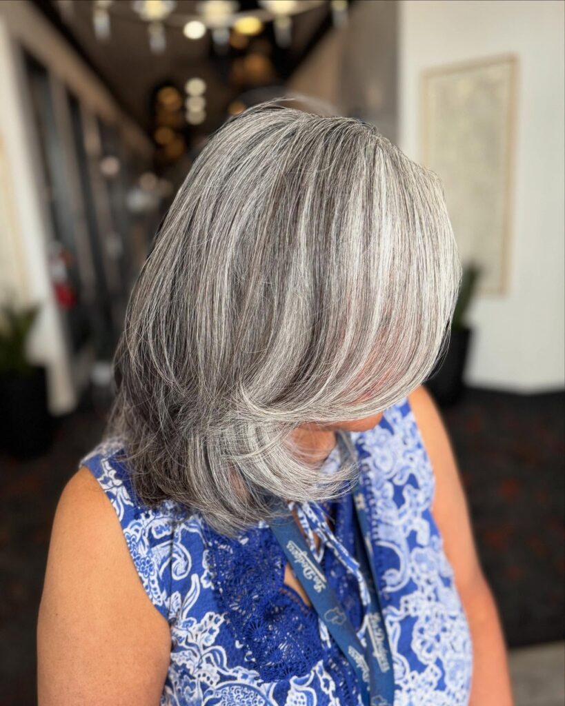 A woman with a shoulder length layered silver and gray bob featuring a sweeping side fringe.