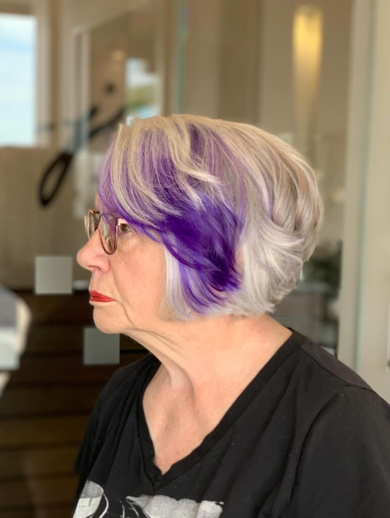 A woman with a silver gray bob featuring bright purple streaks and soft wavy layers.