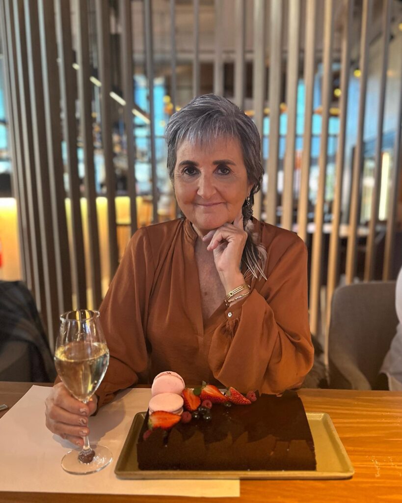 A woman with a short textured slate gray pixie cut sitting at a table with a dessert.