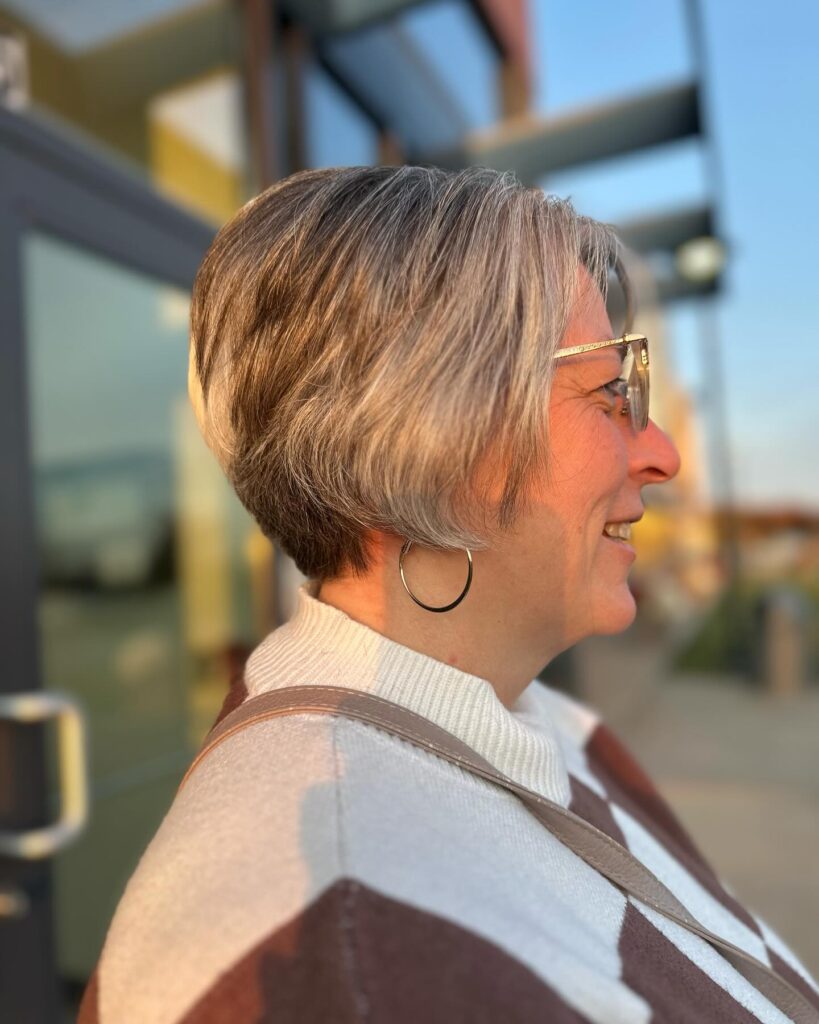 A woman showing a side profile of her short silver and blonde wedge hairstyle with a tapered neckline.