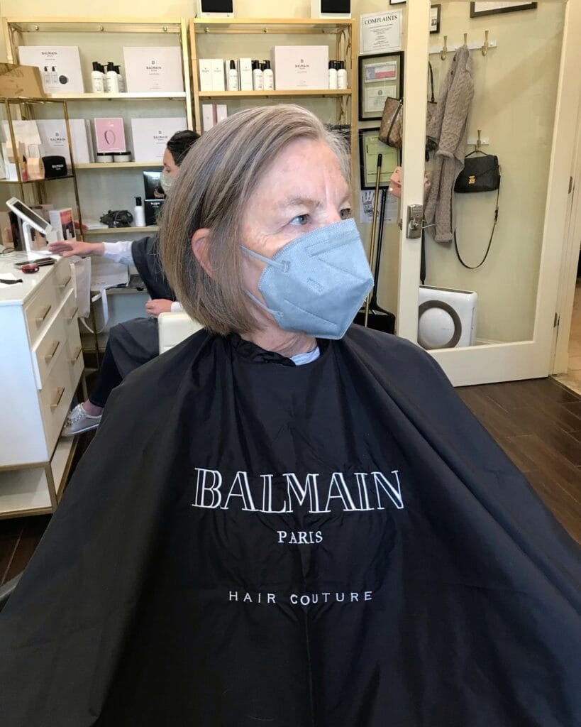 A woman in a salon chair with a straight chin length mushroom brown bob that curves inward at the ends.