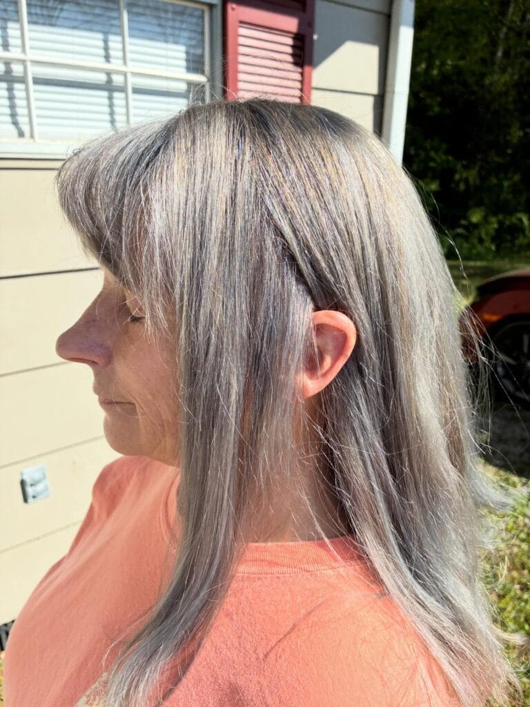 A side profile of a woman with long straight silver hair and light wispy bangs.