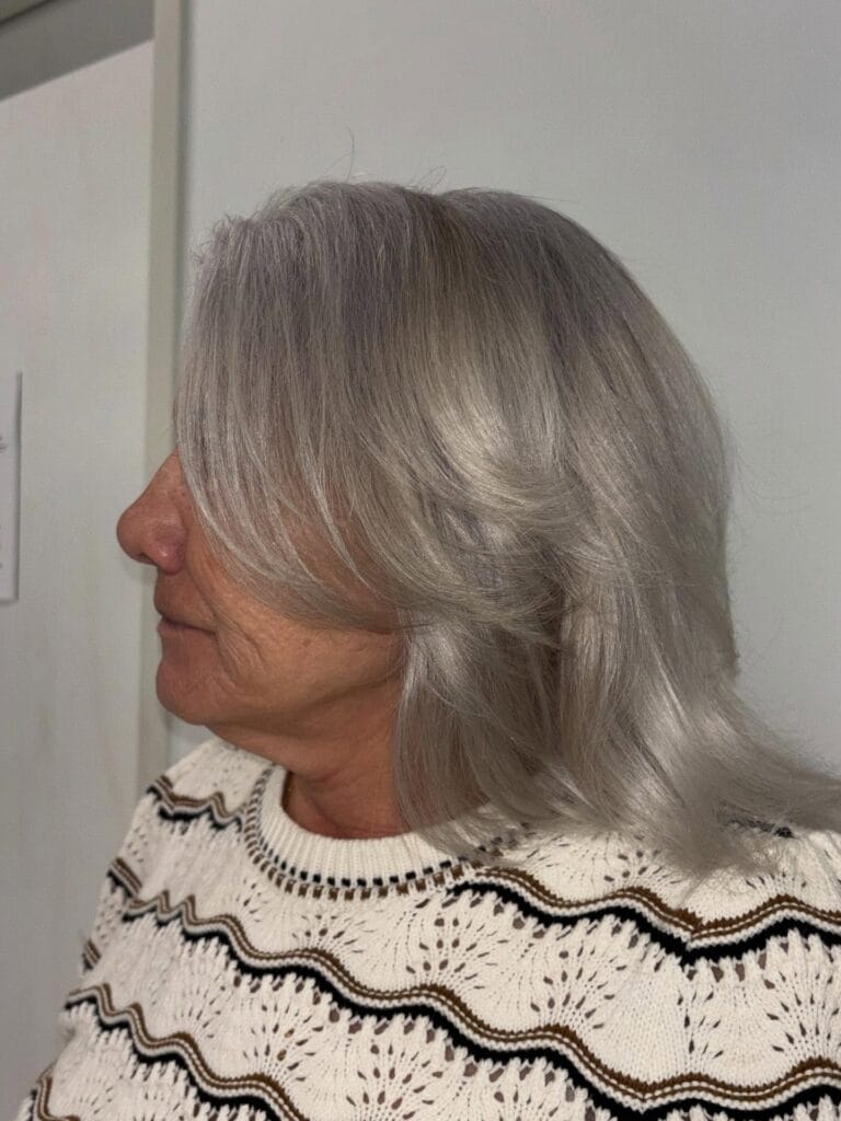 A woman showing the side profile of her shoulder length feathered silver hair with face framing layers.