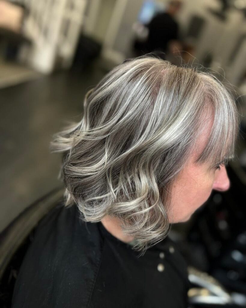 A woman with a wavy chin length bob featuring high contrast silver highlights and salt and pepper lowlights.