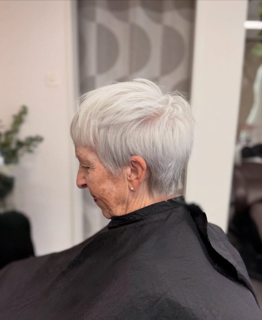 A side profile of a woman with an ultra short textured pixie cut in a bright snowy white color.