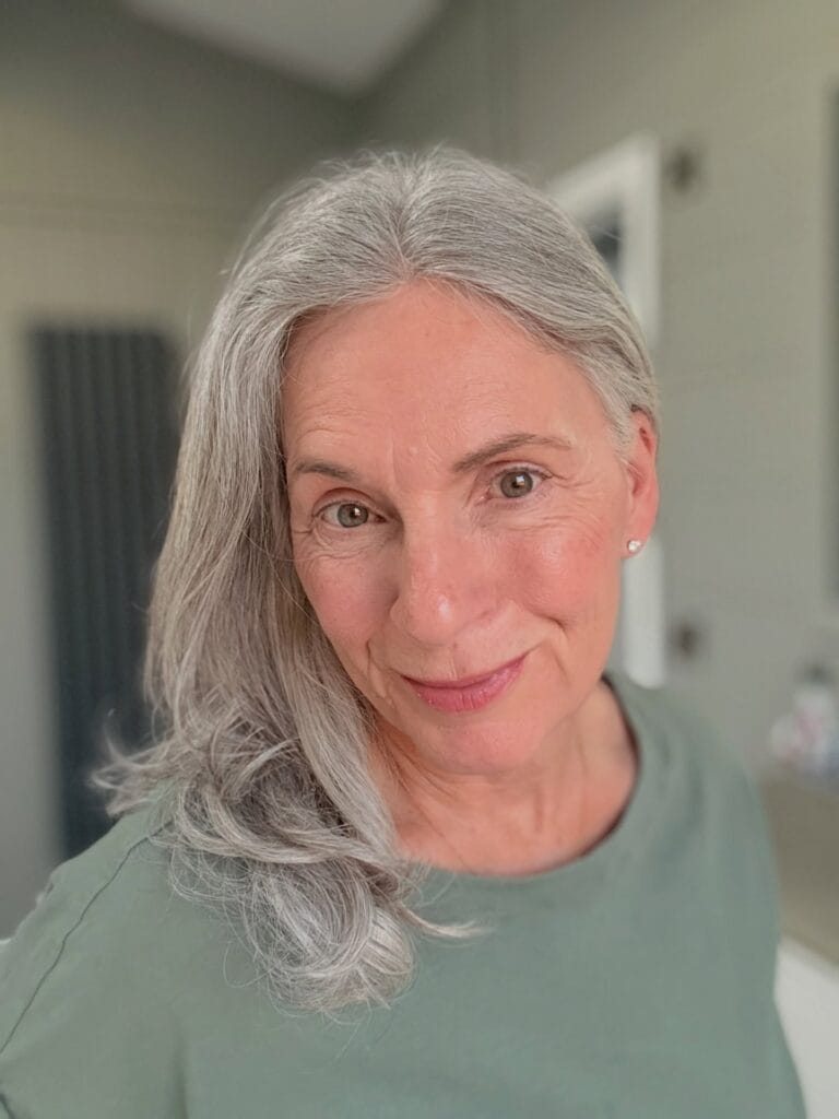 A woman with long silver hair styled with a side tuck and soft curls at the ends.