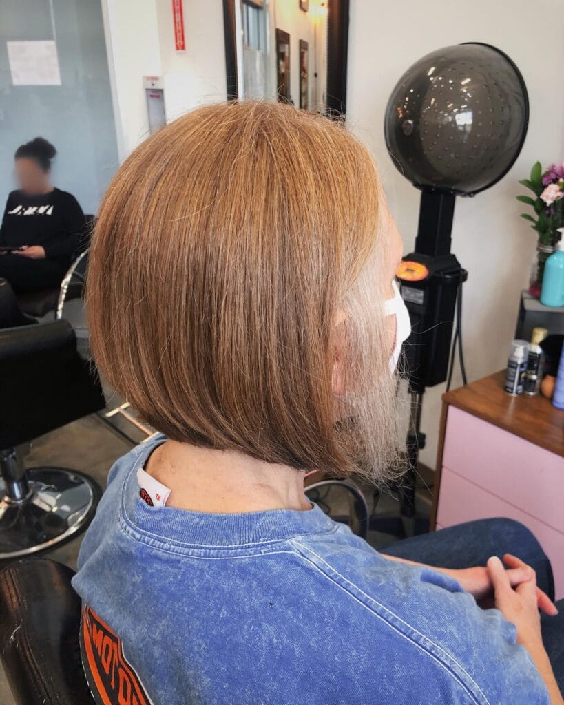 A side profile of a woman with a straight warm caramel A-line bob with soft layers standing in a salon.