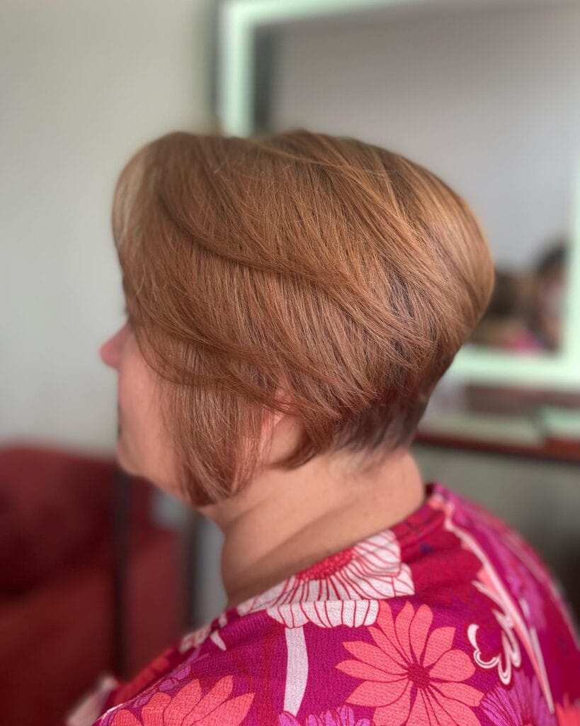 A woman with a short tapered copper red wedge haircut featuring voluminous side swept layers.