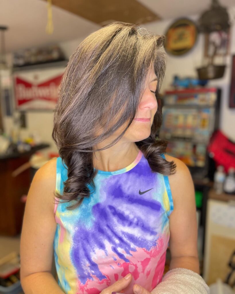 A woman showcases a medium length brunette hairstyle with soft face framing layers and elegant curls at the ends.