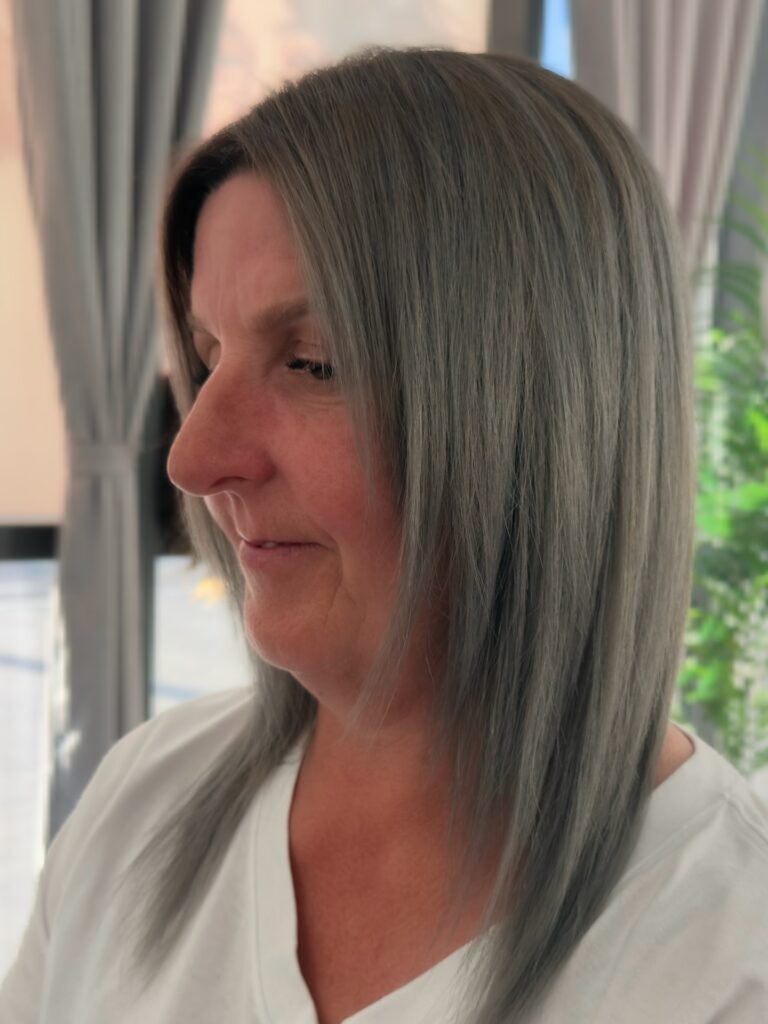 A woman with long straight icy slate grey hair featuring subtle face framing layers and a smooth polished finish.