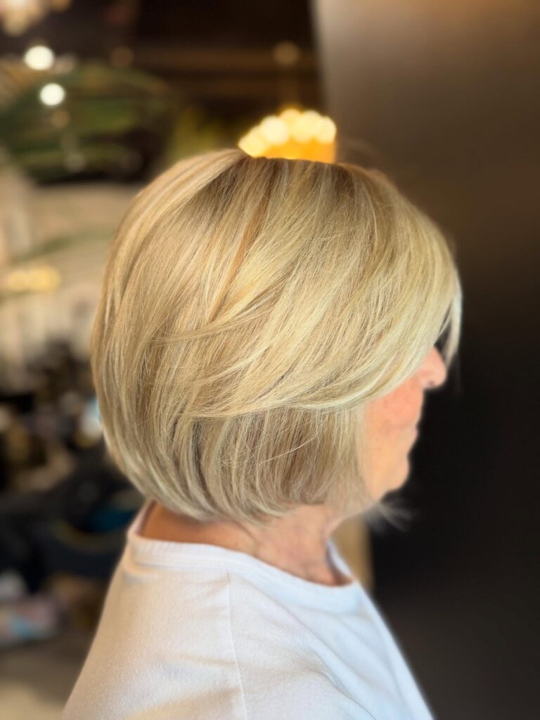 A close up side profile view of a woman with a stacked blonde bob haircut featuring multidimensional golden highlights.
