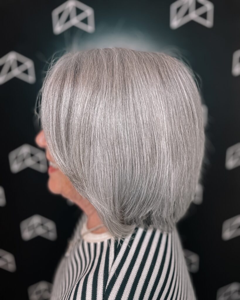 A side profile view of an older woman with a sleek shiny icy silver layered bob haircut that curves slightly towards the jawline.