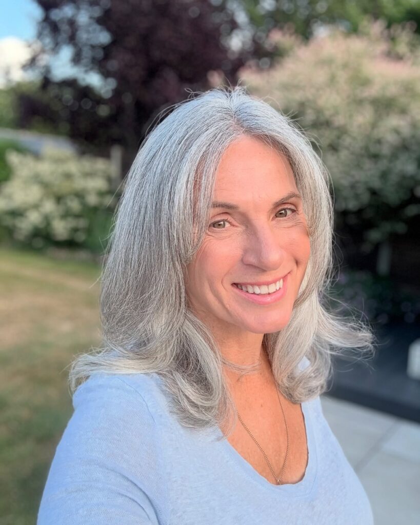 A smiling woman with long natural silver hair featuring soft blended layers and a face framing fringe.