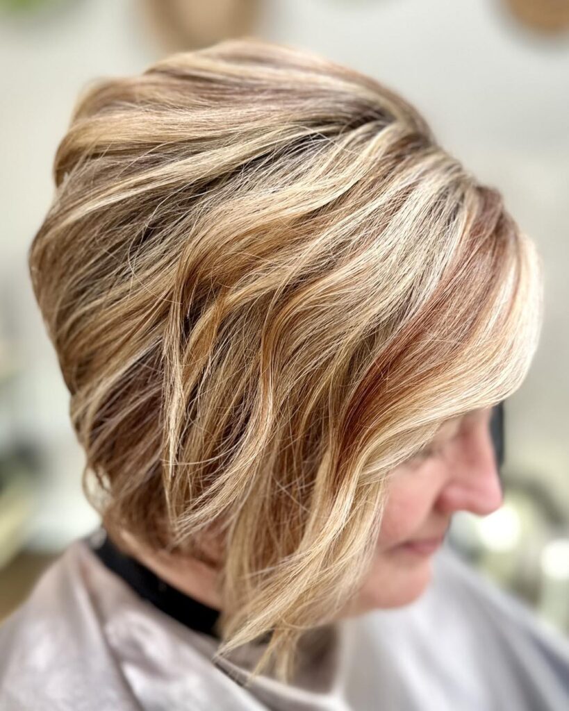 A side profile view of an older woman with a textured stacked inverted bob haircut featuring multi-tonal copper honey and blonde highlights.