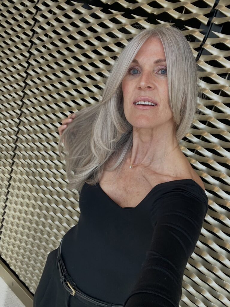 A woman with long silky silver hair styled with a middle part and subtle layers at the ends.