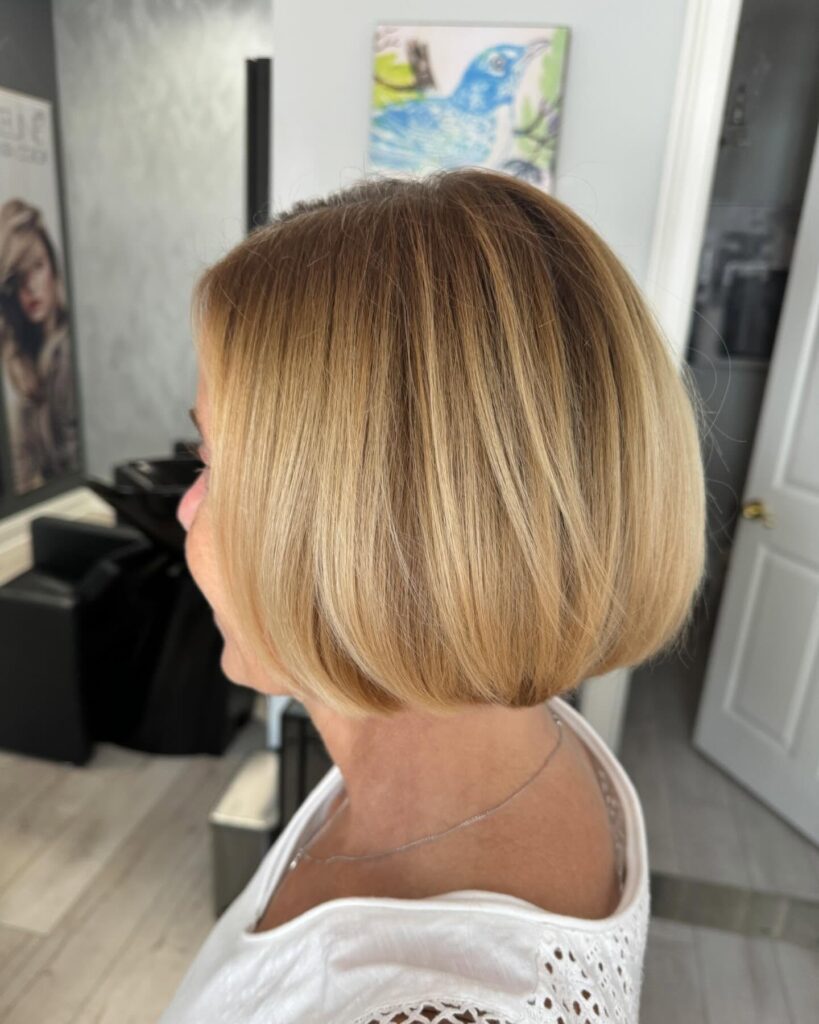 A side profile of a woman with a rounded chin length caramel blonde bob and soft golden highlights.