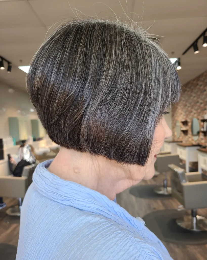 A side view of a woman with a sleek angled bob featuring a natural salt and pepper hair color.