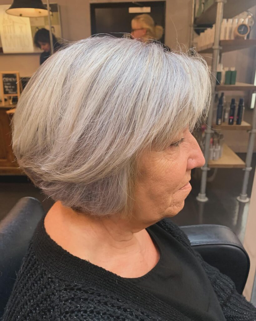 A woman with a short layered silver hairstyle featuring voluminous crown layers and a soft side swept fringe.