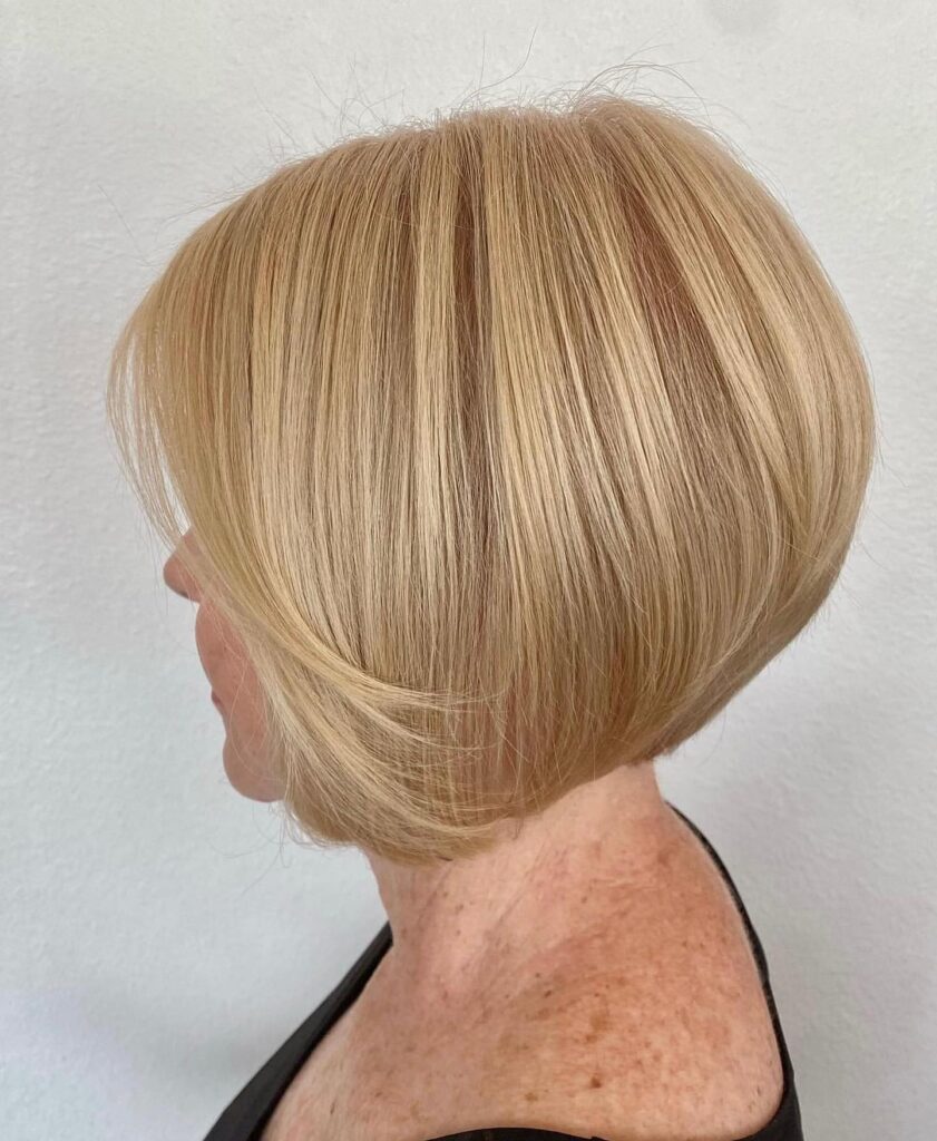 Side view of a woman with a sleek honey blonde inverted bob hairstyle with stacked layers at the back.