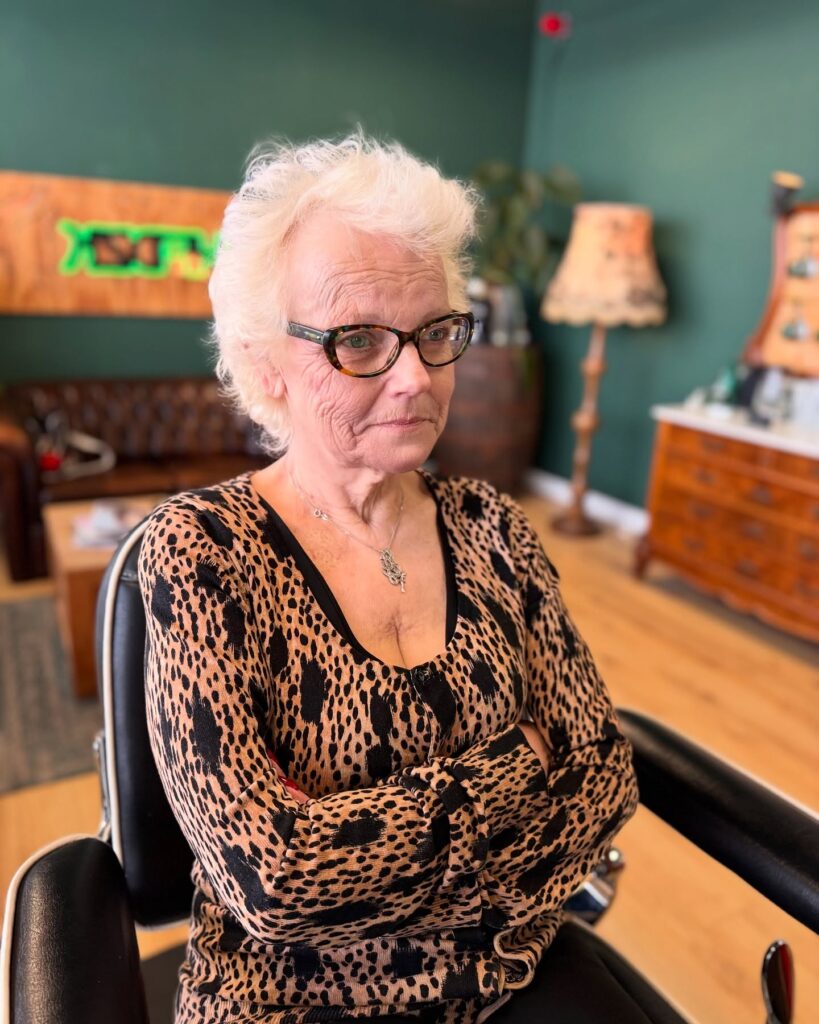 A woman with a voluminous swept back white pixie cut and glasses wearing a leopard print top.