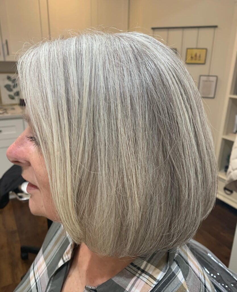 A woman with a rounded chin length bob in a natural salt and pepper silver blend with a smooth texture.